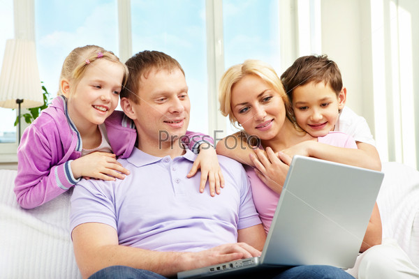 A family of four sitting on sofa and looking at laptop screen