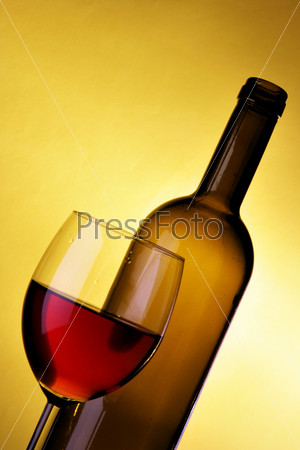 Glass and bottle of red wine over yellow background