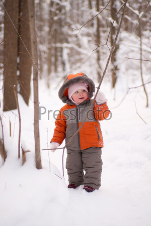 Adorable baby walking in snow winter forest touch wood branch on tree