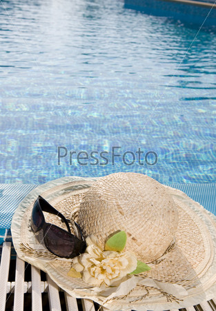 The straw hat and  Sunglasses lies on the brink of pool