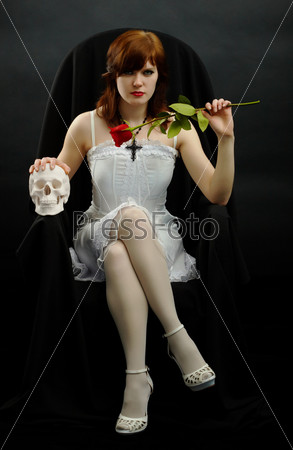 Girl sits in black chair with a rose and skull