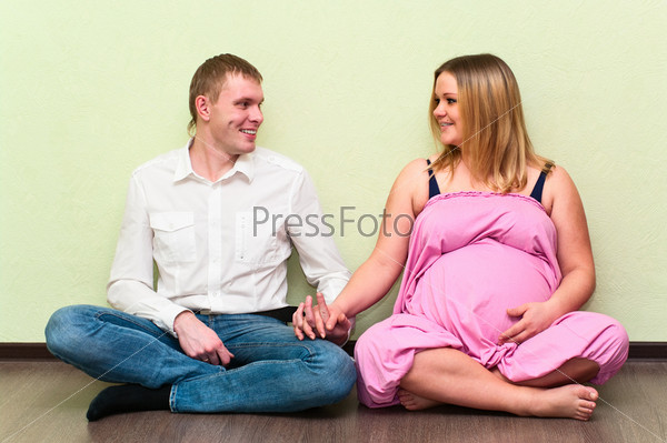 Pregnant woman with her husband sitting on floor in empty room. Caucasians, a loving young couple