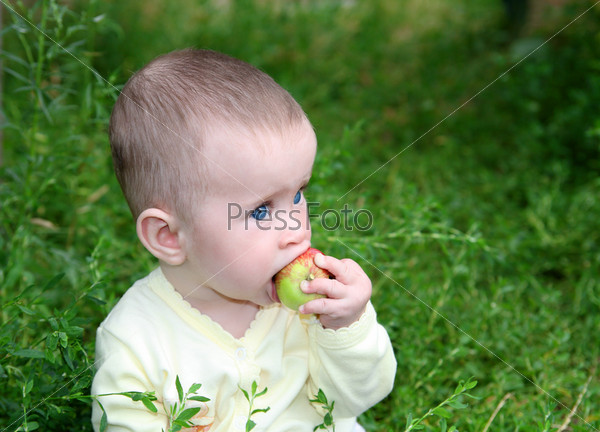 small baby biting apple in green grass