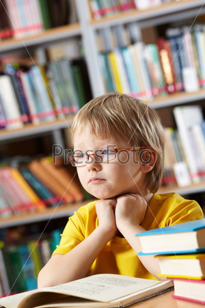 Portrait of clever boy thinking while reading book in library