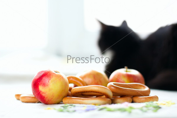 Натюрморт с яблоками, бубликами и силуэтом кота на светлом фоне