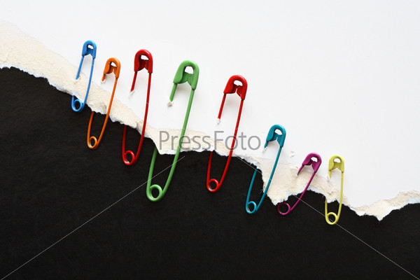 Set of color safety pins attached to disrupt white paper on black background