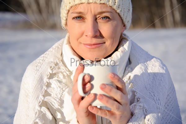 adult woman in white, with mug in his hands  on a snowy background, bright sunny frosty day