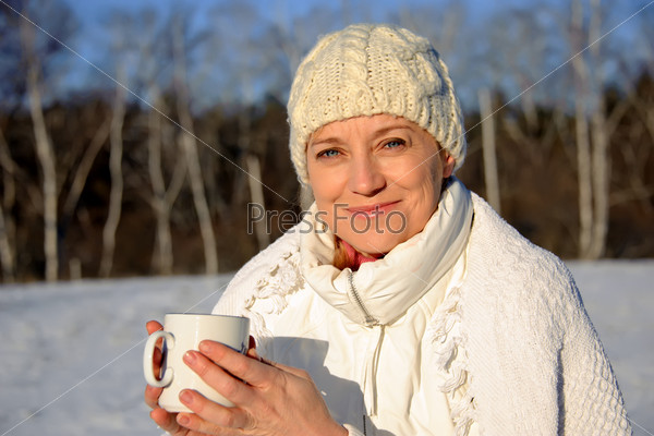 adult woman in white, with mug in his hands  on a snowy background, bright sunny frosty day