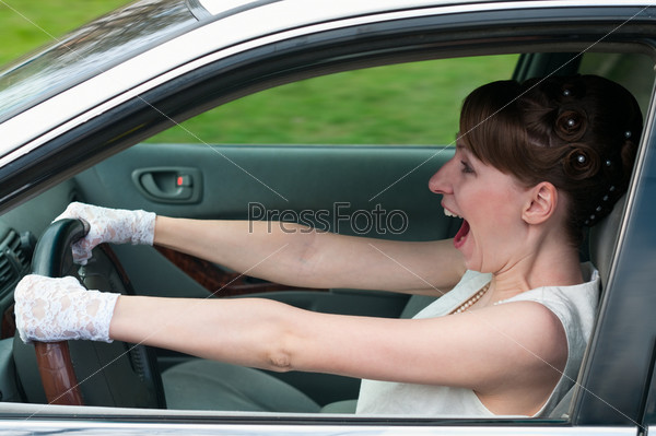 Woman in white dress and white-gloved driving a car and screaming. Looking forward
