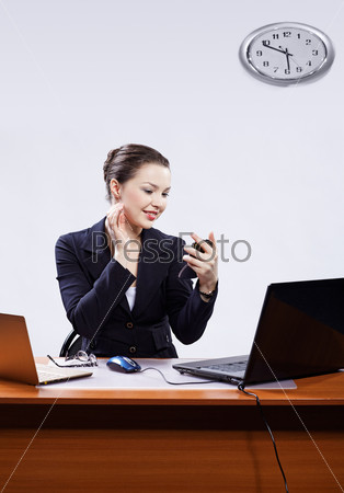 office portrait of beautiful young business woman sitting at her workplace with two laptops on gray checking makeup