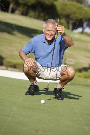 Senior Male Golfer On Golf Course Lining Up Putt On Green
