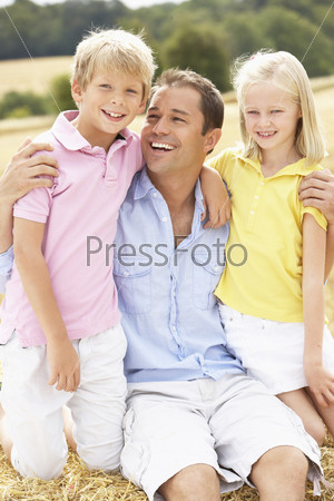 Father And Children Sitting On Straw Bales In Harvested Field