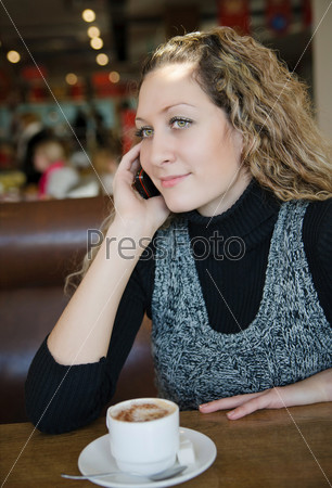beautiful girl with blond curly hair talking on a cell phone in cafe