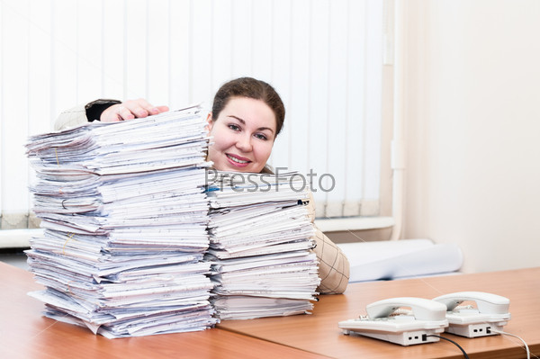 Woman sitting at the table in working place in office room with lot of papers