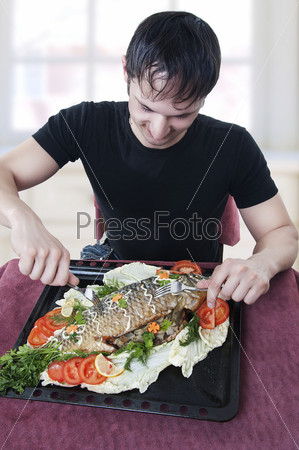 hungry young man waiting to eat freshly roasted stuffed fish with two forks on light kitchen at home