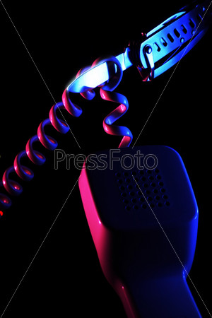 Attempt to cut spiral shaped wire of the telephone handset by swiss knife illuminated by blue and pink colored light sources on the black background