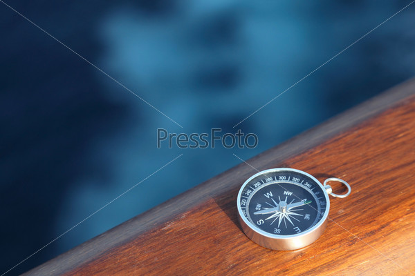 Little cruise compass on wooden rail sea on background