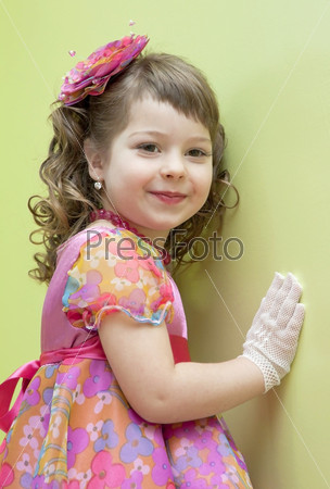 The elegant girl in a dress and gloves costs near a wall