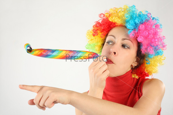 young beauty woman in clown wig and party blower pointing left, half body