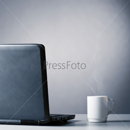 Ноутбук и чашка горячего кофе на столе