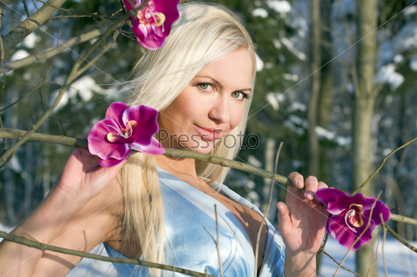 Woman with orchid in the winter forest. She is dressed only in silk gown