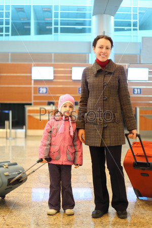 Mother and girl with suitcases standing at airport