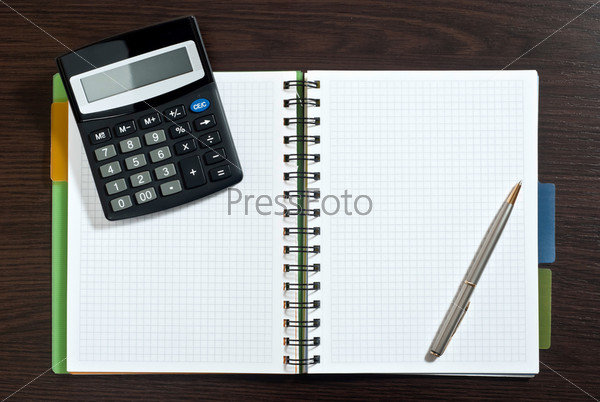 Notebook, ballpen and calculator on dark wooden desk