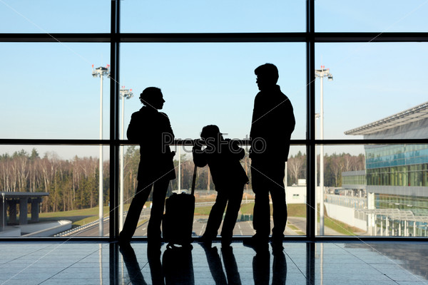 silhouette of mother, father and son with luggage standing near window in airport