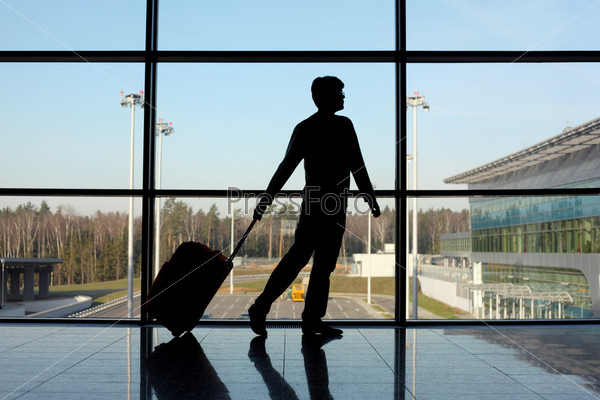 silhouette of man with luggage walking right near window in airport