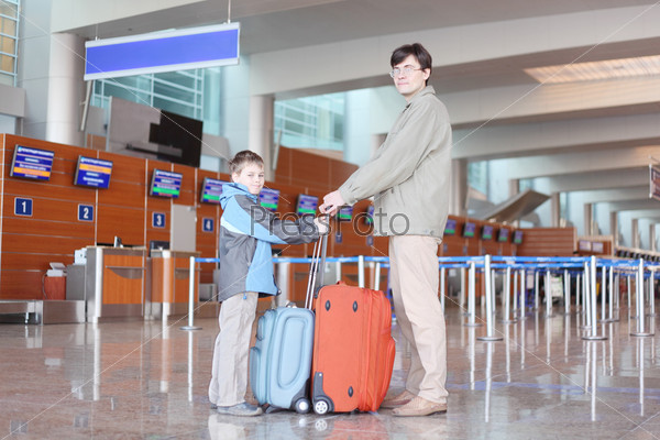 father and son with red suitcase standing in airport hall side view looking at camera