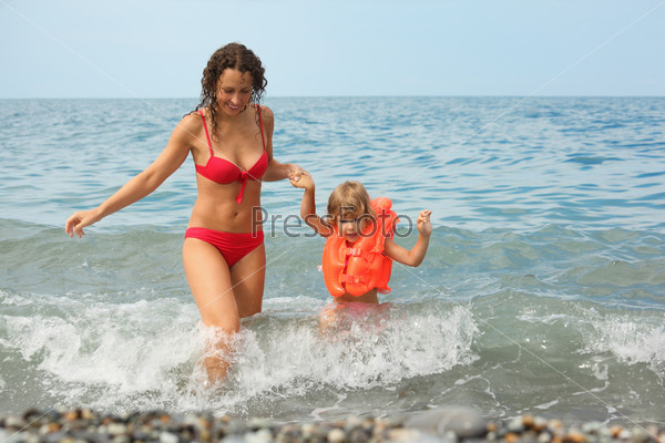attractive woman with her daughter in water. little girl wearing life-jacket.