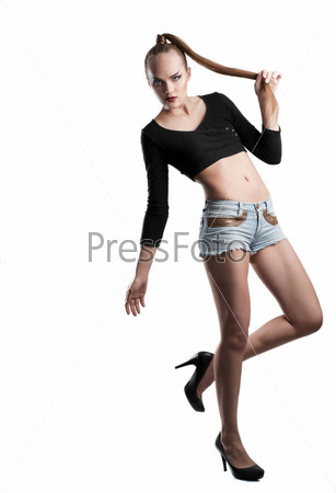 Fashion studio shot of young and beautiful woman holding her hair in hand. Wearing black blouse, blue jean shorts and black shoes, on white background. (Professional makeup and hair style).