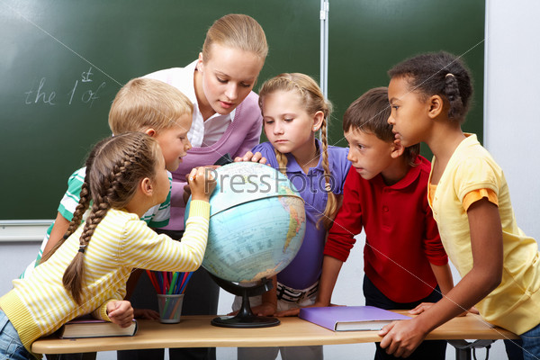 Portrait of pupils looking at globe while listening to teacher during geography lesson, stock photo