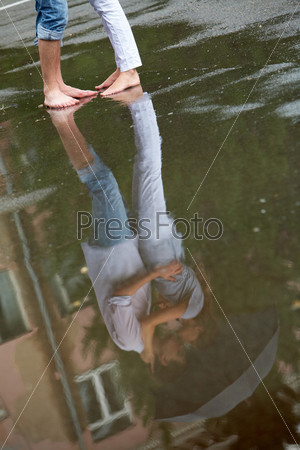 Reflection in puddle of woman and man embracing under umbrella during rain