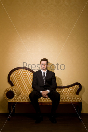 businessman in suit sitting on sofa in room, combined hands together
