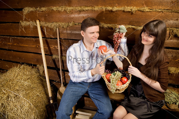 smiling man and young woman with basket of fruit sitting on bench in wooden log hut