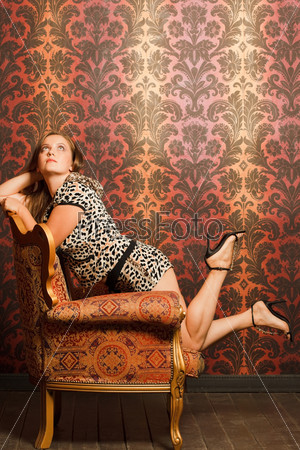 woman in spot cat clothes in  vintage chair looks up. red-yellow pattern wallpaper and wooden floor