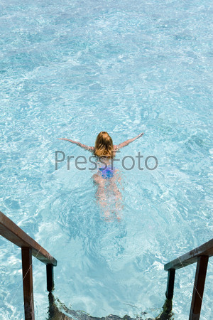 Maldives.  Young sports woman swims from steps of villa on water.