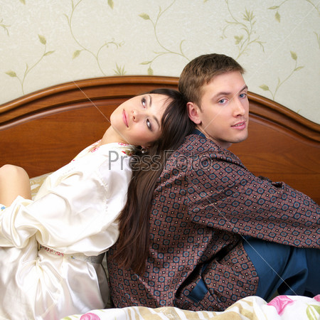 Young happy couple sitting back to back on the bed