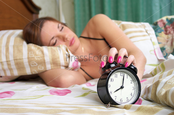 Young sleeping female turns alarm clock off  (woman out of focus)