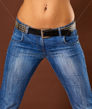 A young woman in jeans - close-up belly and hips on brown background
