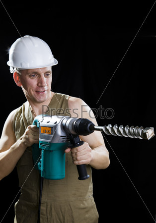 The builder in a protective helmet holds the professional puncher-hammer with a drill of the big diameter