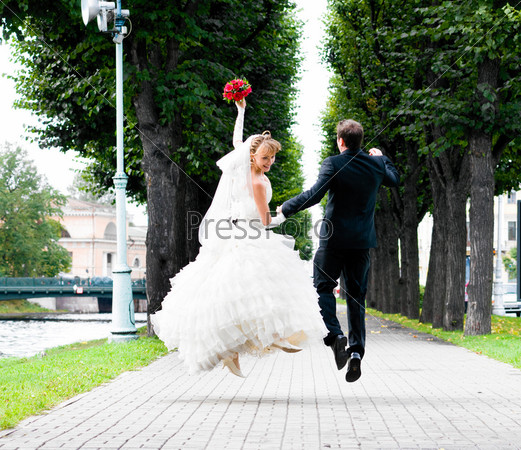 bride and groom is running with joined hands on city park road