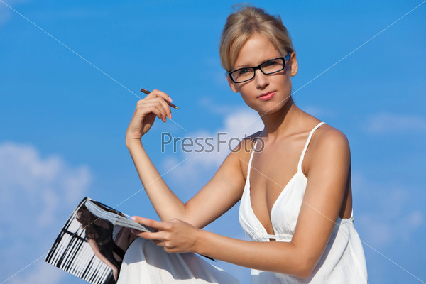 The girl wearing spectacles sits on a blue background of the sea and reads