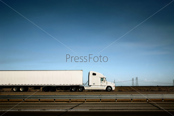 White freight truck driving on freeway under blue sky.