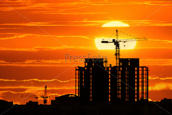 Construction project silhouette against sunset sky with big sun setting down