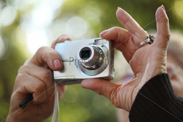 Senior female hands holding compact point-n-shoot photo camera, shooting outdoors. Closeup, shallow DOF