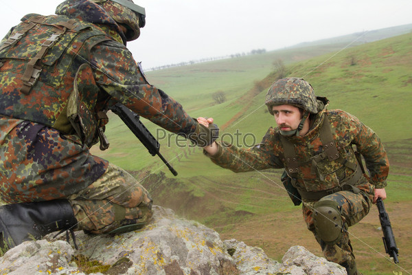 Military man helping his friend to climb up the rock