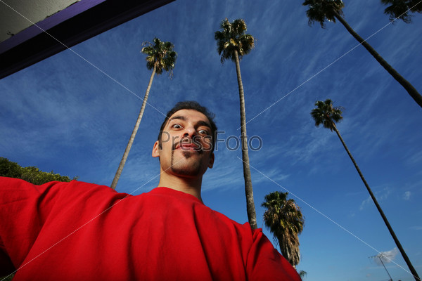 Portrait of a young man in California, blue sky and palm trees behind him.