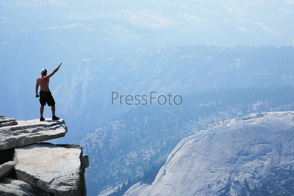 Man standing on top of a cliff with arm raised
